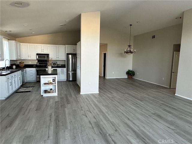 kitchen featuring a sink, white cabinets, open floor plan, appliances with stainless steel finishes, and dark countertops