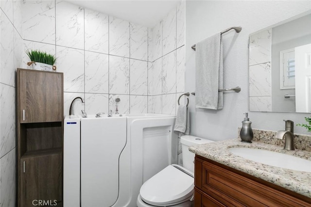 bathroom with toilet, tile walls, and vanity