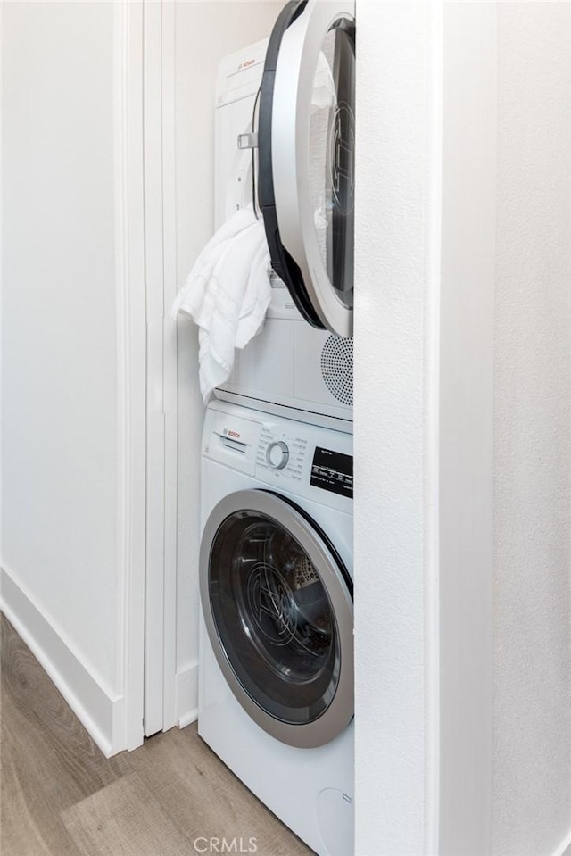 clothes washing area with light hardwood / wood-style flooring and stacked washing maching and dryer