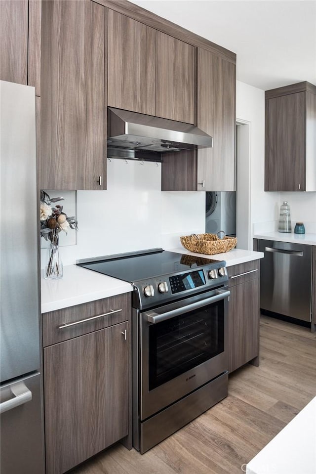 kitchen with light wood-type flooring, wall chimney range hood, and stainless steel appliances