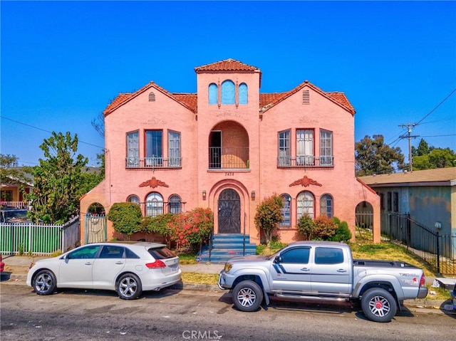 view of front of home featuring a tile roof, fence, a balcony, and stucco siding