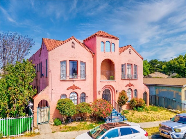 mediterranean / spanish-style home with a fenced front yard, a tile roof, and stucco siding