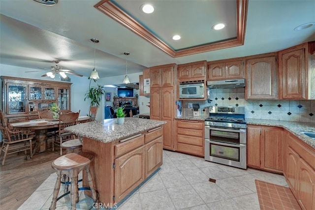 3067 Trinity Dr, Costa Mesa, CA 92626 - kitchen with under cabinet range hood, a center island, decorative backsplash, appliances with stainless steel finishes, and ceiling fan