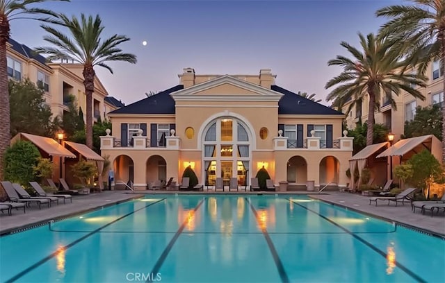 back of property with a balcony, a patio area, a community pool, and stucco siding