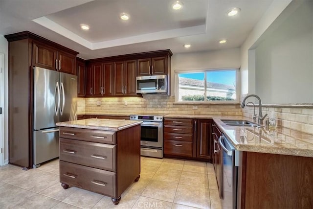 kitchen with a raised ceiling, backsplash, appliances with stainless steel finishes, a sink, and light stone countertops