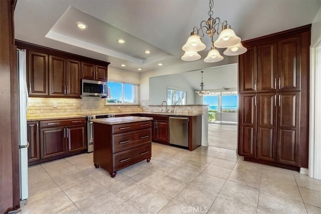 kitchen featuring a tray ceiling, stainless steel appliances, backsplash, a chandelier, and a peninsula