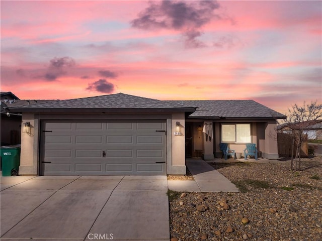 ranch-style home featuring an attached garage, driveway, a shingled roof, and stucco siding