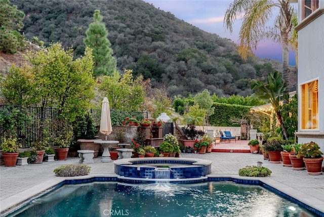 pool at dusk featuring a deck with mountain view, an in ground hot tub, and a patio area