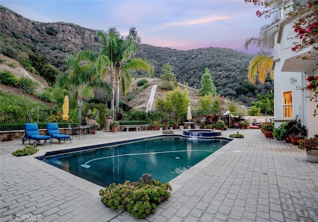 pool at dusk featuring an in ground hot tub, a mountain view, and a patio