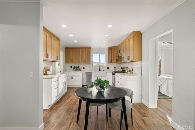 kitchen featuring crown molding, decorative backsplash, wood finished floors, baseboards, and appliances with stainless steel finishes