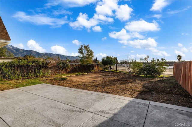 view of yard featuring fence, a mountain view, and a patio