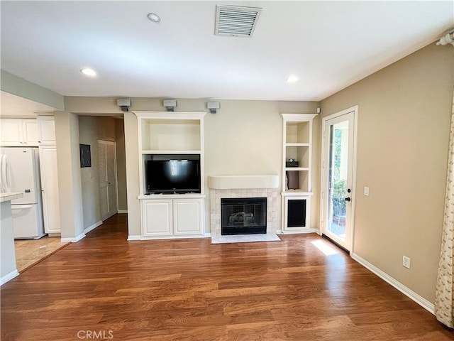 unfurnished living room featuring built in shelves, wood finished floors, visible vents, and baseboards