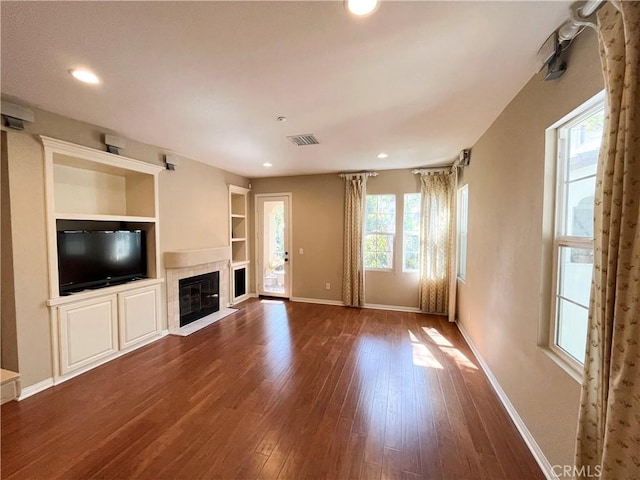 unfurnished living room with a tile fireplace, dark wood-type flooring, and built in features