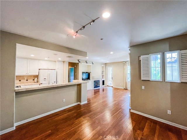 kitchen with baseboards, tile counters, dark wood-type flooring, white refrigerator with ice dispenser, and white cabinetry