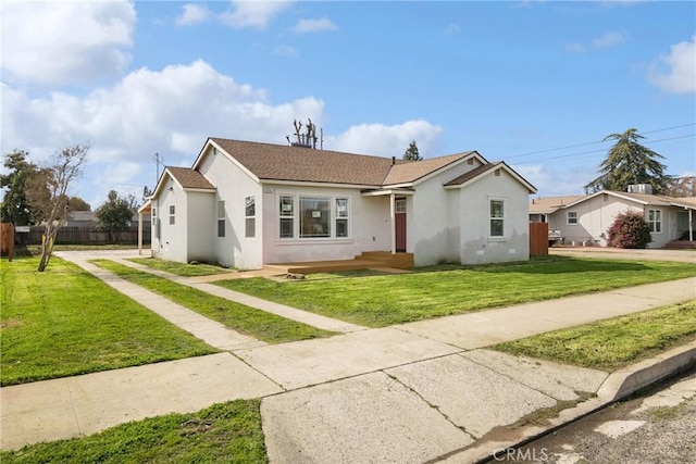 view of front of home with stucco siding, a front yard, and fence