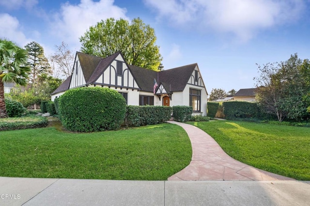 english style home featuring roof with shingles, a front lawn, and stucco siding