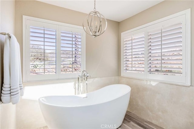 bathroom with a chandelier, a soaking tub, a healthy amount of sunlight, and wood finished floors