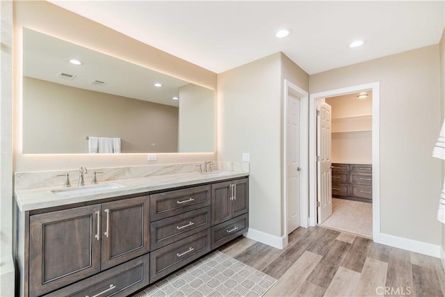 full bath with double vanity, a walk in closet, a sink, and wood finished floors