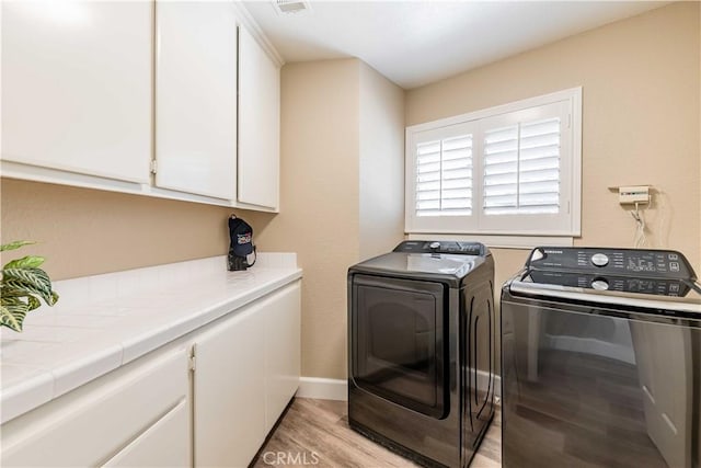 washroom with cabinet space, visible vents, baseboards, washer and clothes dryer, and light wood-style flooring