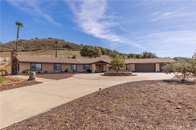 ranch-style home with driveway, a chimney, an attached garage, and stucco siding