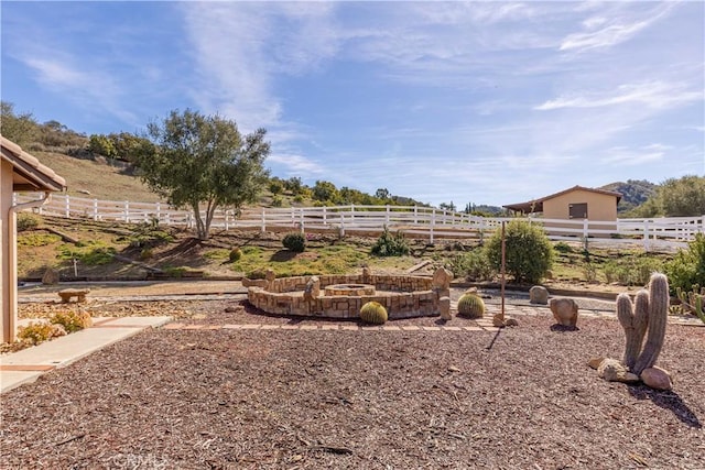 view of yard with an outdoor fire pit, fence, and a rural view