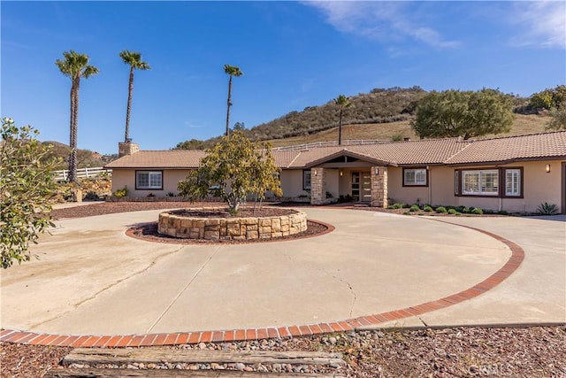 single story home featuring a mountain view, curved driveway, a tile roof, stucco siding, and a chimney