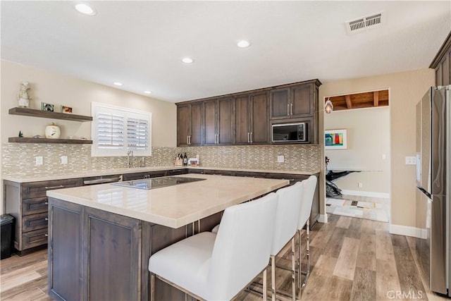 kitchen with a kitchen island, freestanding refrigerator, built in microwave, black electric cooktop, and light countertops