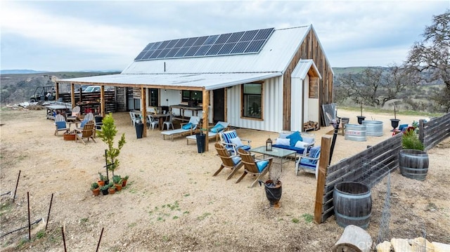 back of house with a patio, an outdoor fire pit, solar panels, board and batten siding, and metal roof