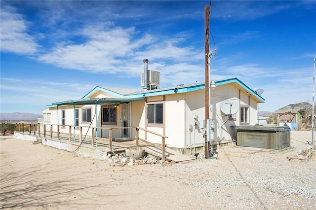 back of property with a mountain view and a hot tub