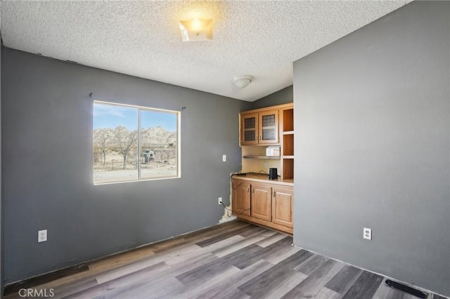 empty room featuring vaulted ceiling, dark wood-type flooring, and a textured ceiling