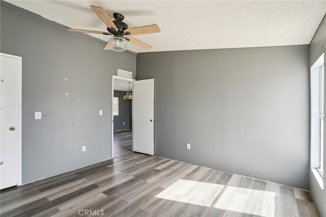 unfurnished bedroom with ceiling fan, vaulted ceiling, a textured ceiling, and hardwood / wood-style floors