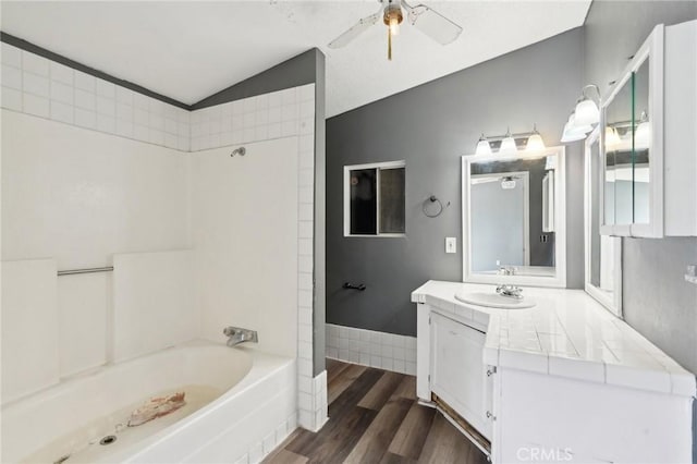 bathroom featuring hardwood / wood-style flooring, ceiling fan, vaulted ceiling, vanity, and tub / shower combination