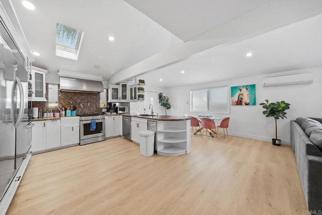 kitchen featuring appliances with stainless steel finishes, wall chimney range hood, sink, white cabinetry, and kitchen peninsula