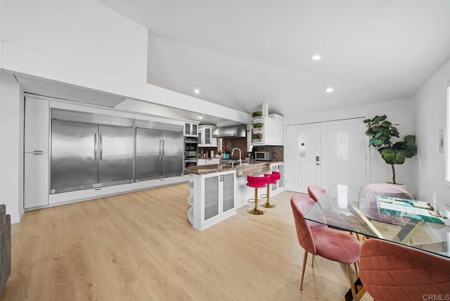 kitchen featuring light stone counters, white cabinetry, light hardwood / wood-style floors, wall chimney exhaust hood, and decorative backsplash