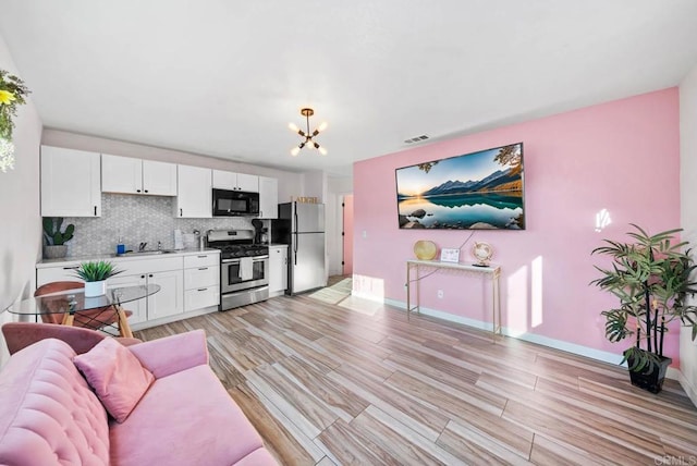 kitchen with tasteful backsplash, stainless steel appliances, white cabinetry, and light wood-type flooring