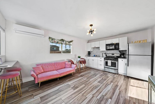 kitchen with an AC wall unit, stainless steel appliances, backsplash, white cabinets, and a chandelier