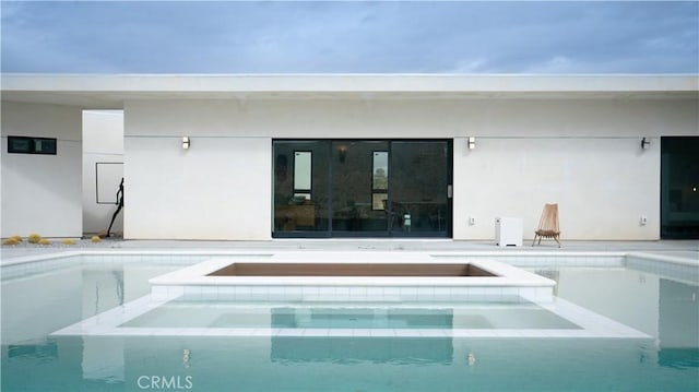 back of house featuring a patio, a pool with connected hot tub, and stucco siding