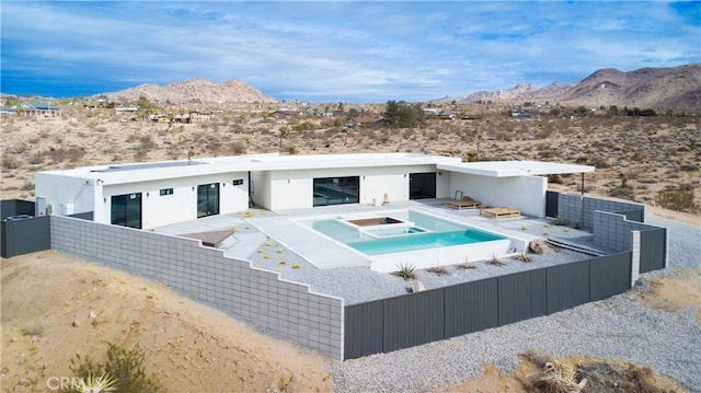 8750 Desert Shadows, Joshua Tree, CA 92252 - back of property featuring an in-ground hot tub, a mountain view, view of desert landscape, and stucco siding