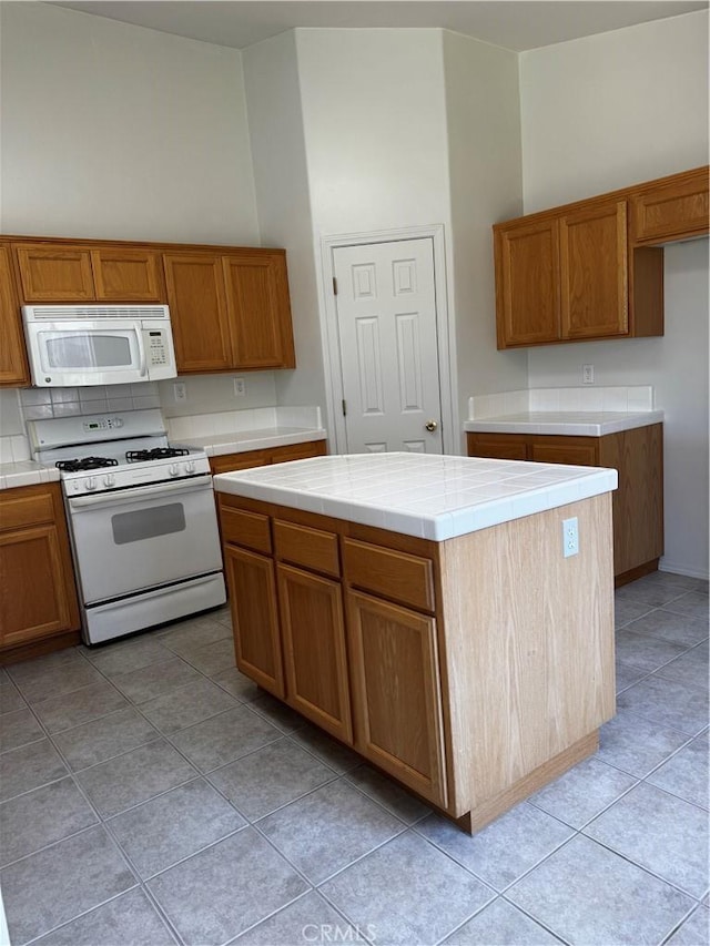 kitchen with light tile patterned floors, white appliances, a towering ceiling, tile counters, and a kitchen island