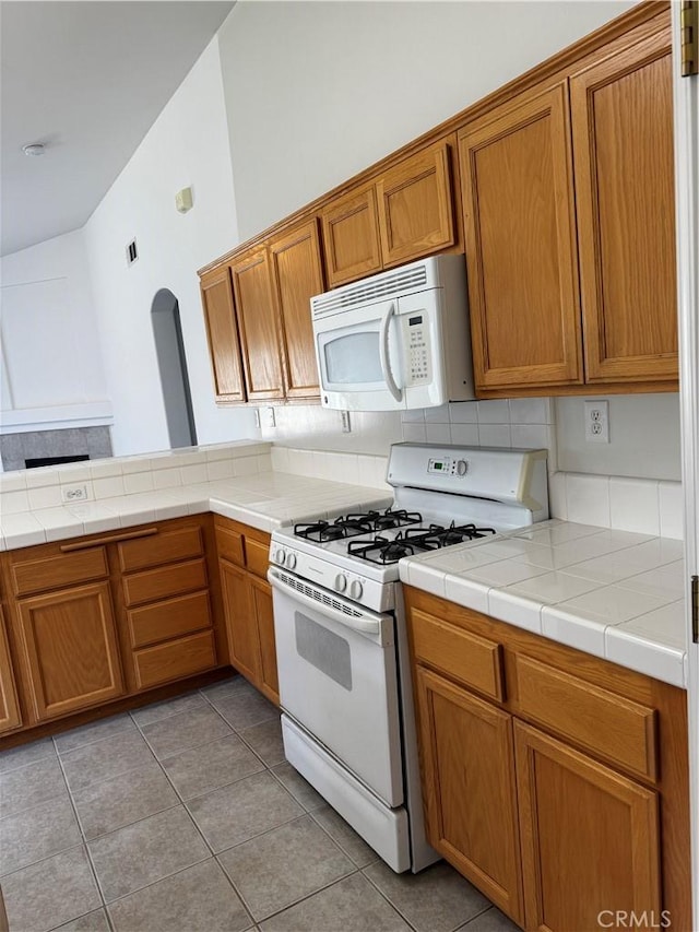 kitchen with white appliances, lofted ceiling, light tile patterned flooring, tile countertops, and tasteful backsplash