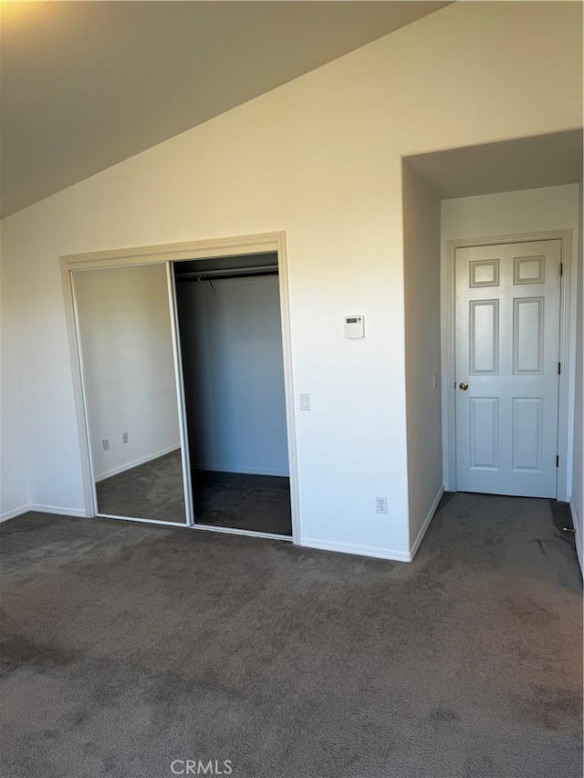 unfurnished bedroom featuring dark carpet, lofted ceiling, and a closet