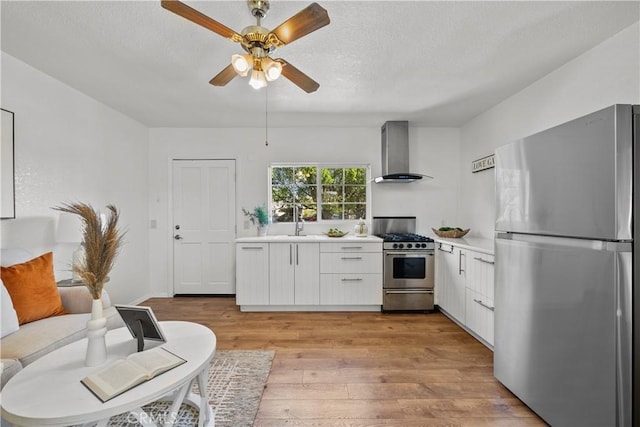 kitchen with stainless steel appliances, white cabinets, wall chimney range hood, light hardwood / wood-style floors, and sink