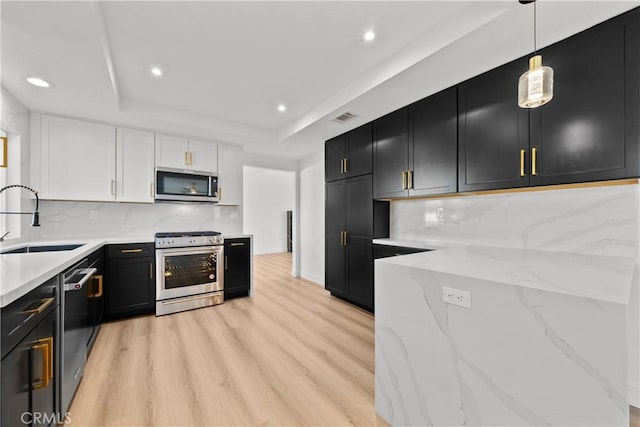 kitchen featuring appliances with stainless steel finishes, pendant lighting, a raised ceiling, sink, and white cabinetry