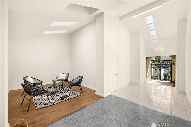 sitting room with light tile patterned flooring, high vaulted ceiling, a skylight, and beam ceiling