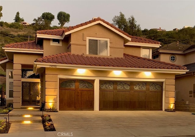 mediterranean / spanish home featuring driveway, a garage, french doors, and stucco siding