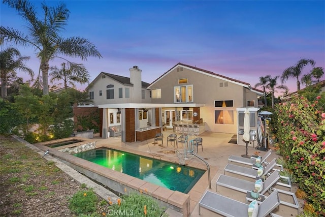 rear view of house featuring an outdoor pool, stucco siding, outdoor dry bar, and a patio