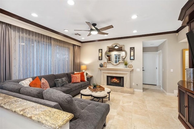 living area featuring crown molding, recessed lighting, a ceiling fan, a warm lit fireplace, and baseboards