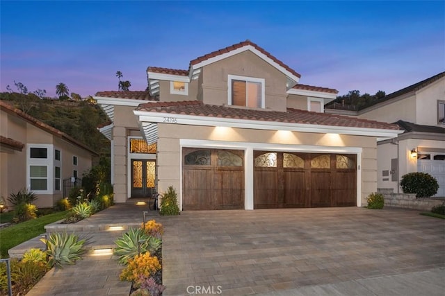 mediterranean / spanish home with a garage, decorative driveway, a tile roof, and stucco siding