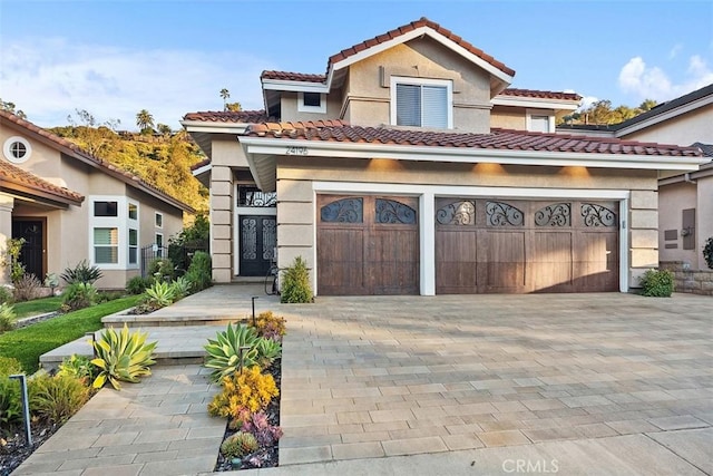 mediterranean / spanish home featuring a garage, decorative driveway, a tile roof, and stucco siding