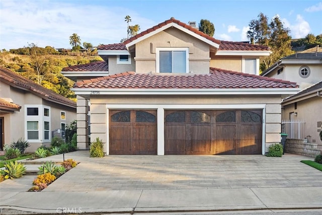 mediterranean / spanish-style home with a garage, decorative driveway, a tile roof, and stucco siding